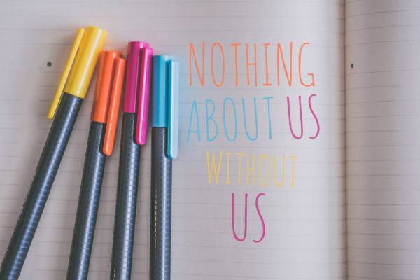 Coloured pens sit next to the written words Nothing About Us, Without Us.