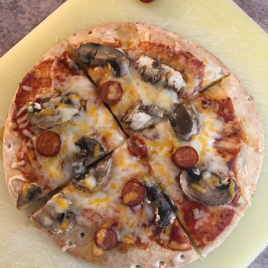 A small pizza cut in four pieces with pepperoni, cheese, and mushrooms. This is one of the cooking activities that the youth centre has done in the past.